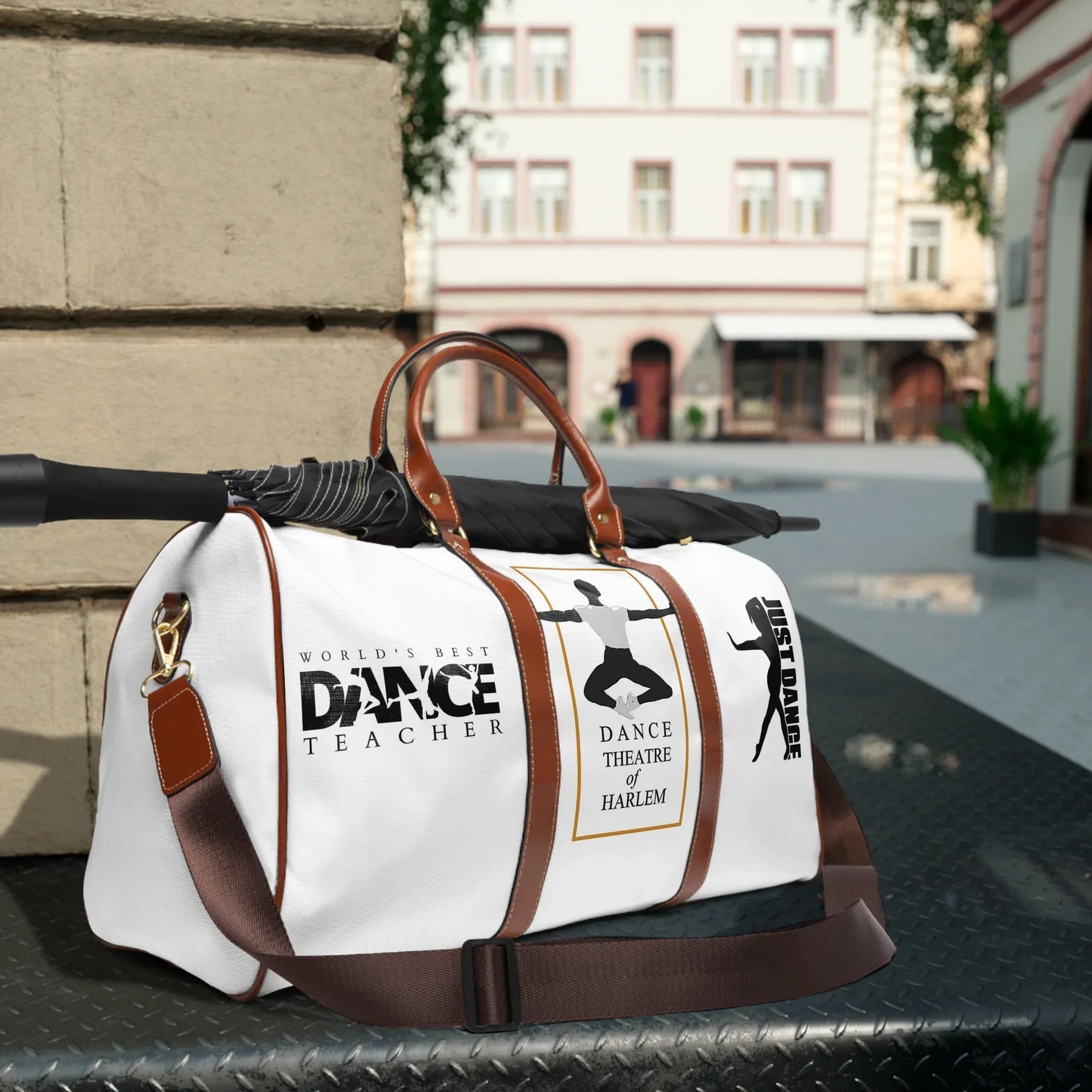 White dance duffel bag with brown straps, black umbrella, and dance-themed prints in city street setting