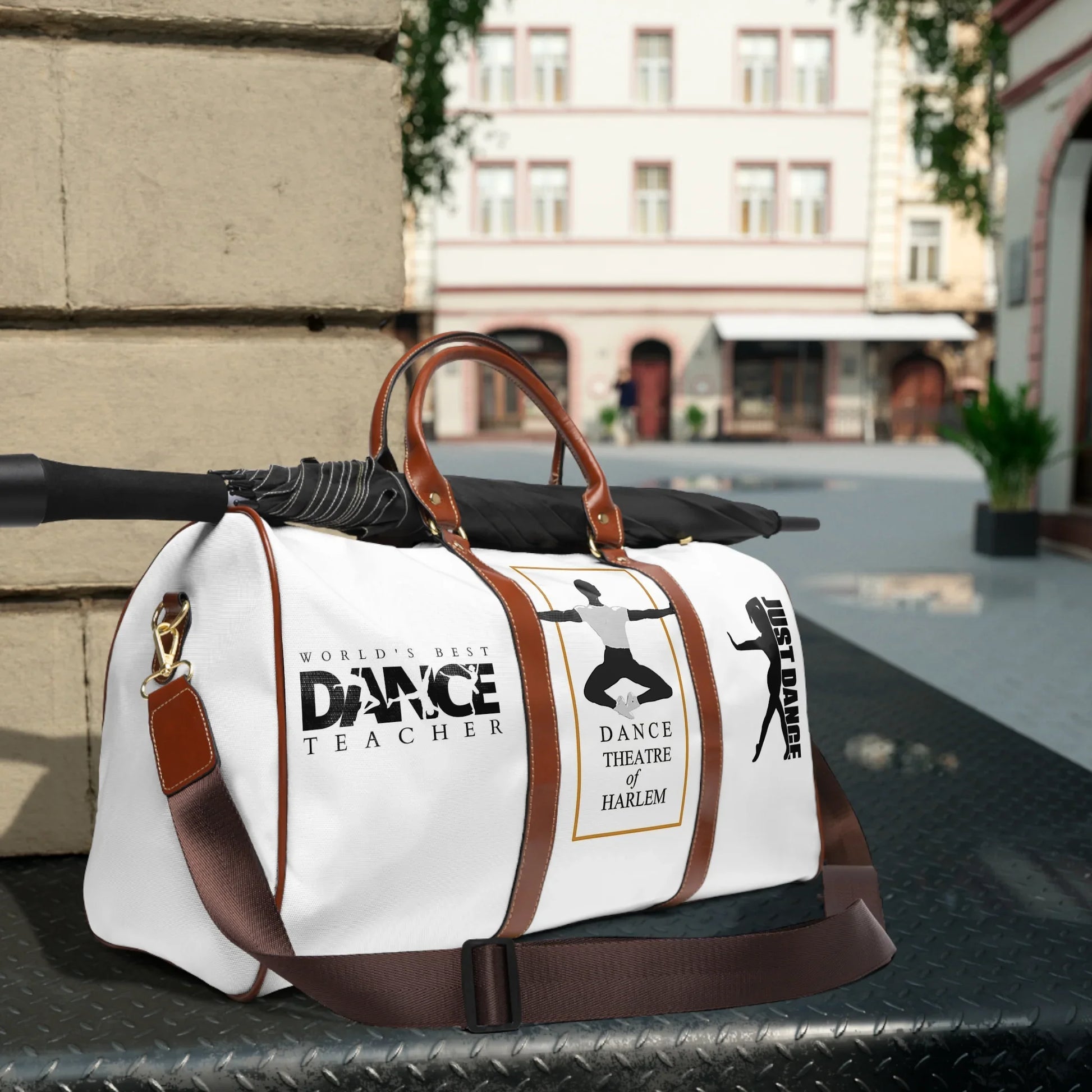 White dance duffel bag with brown straps, black umbrella, and dance-themed prints in city street setting