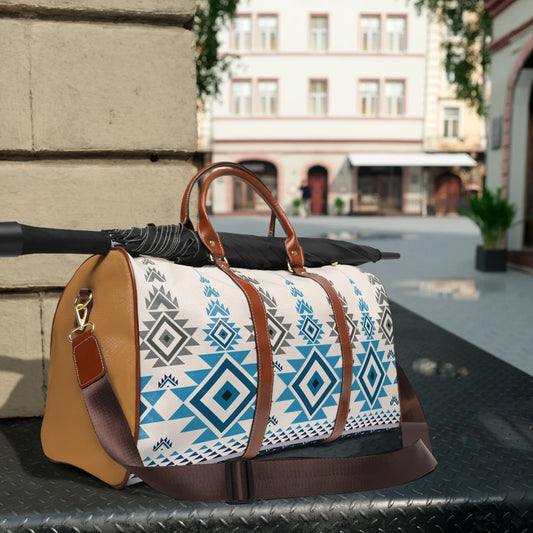 Travel duffel bag with blue and gray geometric pattern and leather straps, resting on metal surface with umbrella